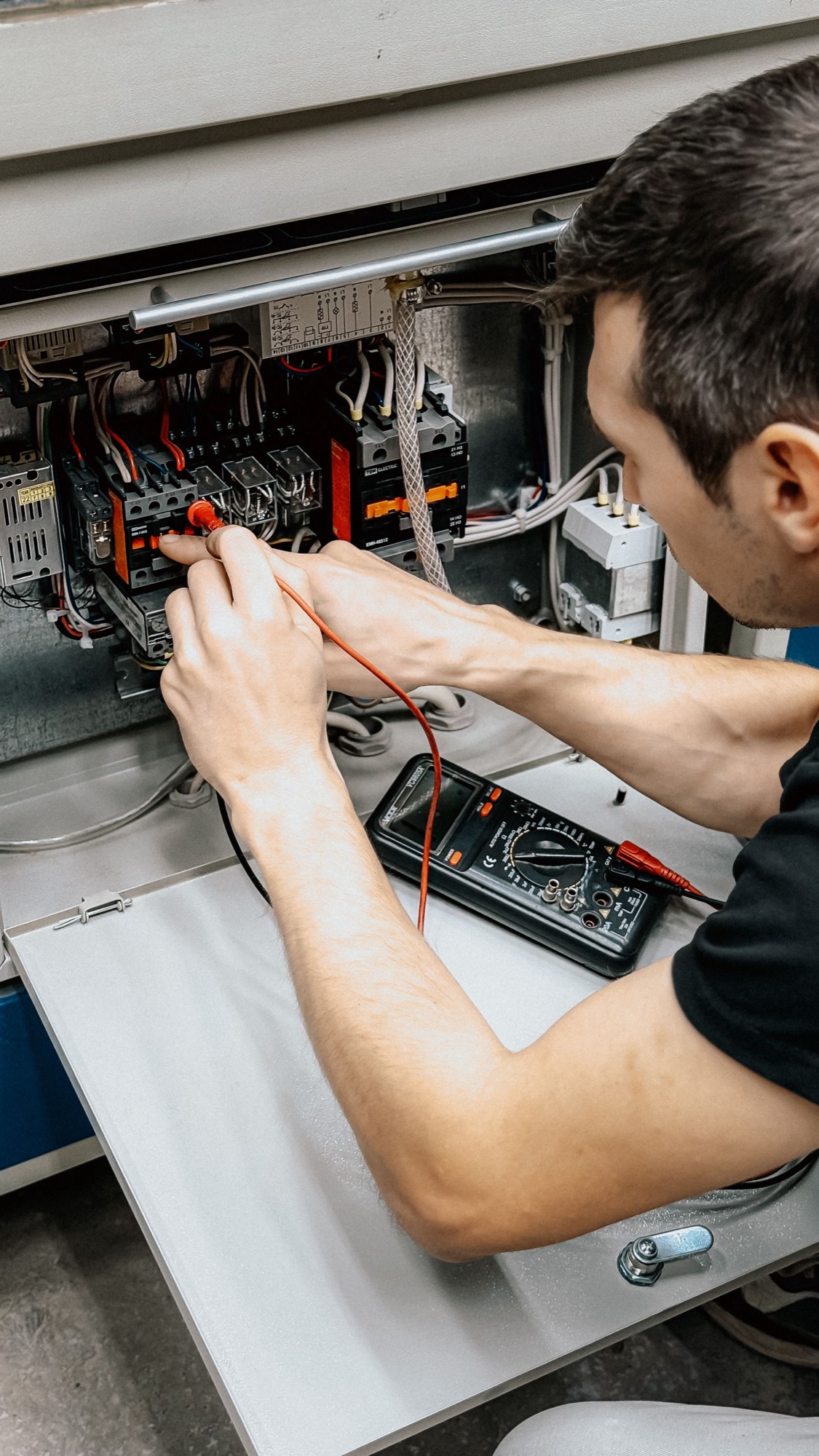An electrician testing connections inside an enclosure with a multimeter