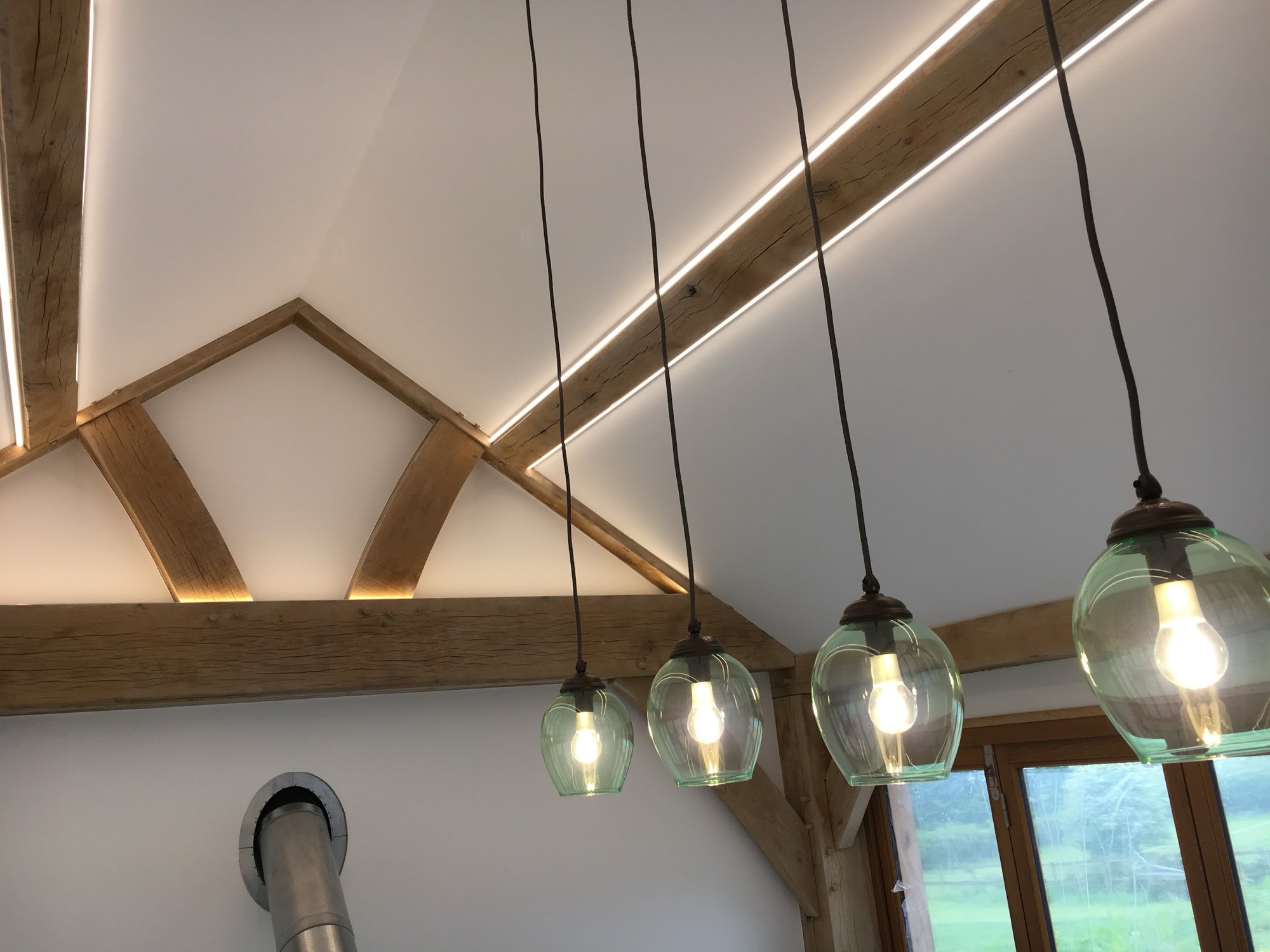 Smoked-glass pendants dropped in a line down an oak frame, wired back to a single dimmed circuit, with concealed strip picking out the beams behind them.