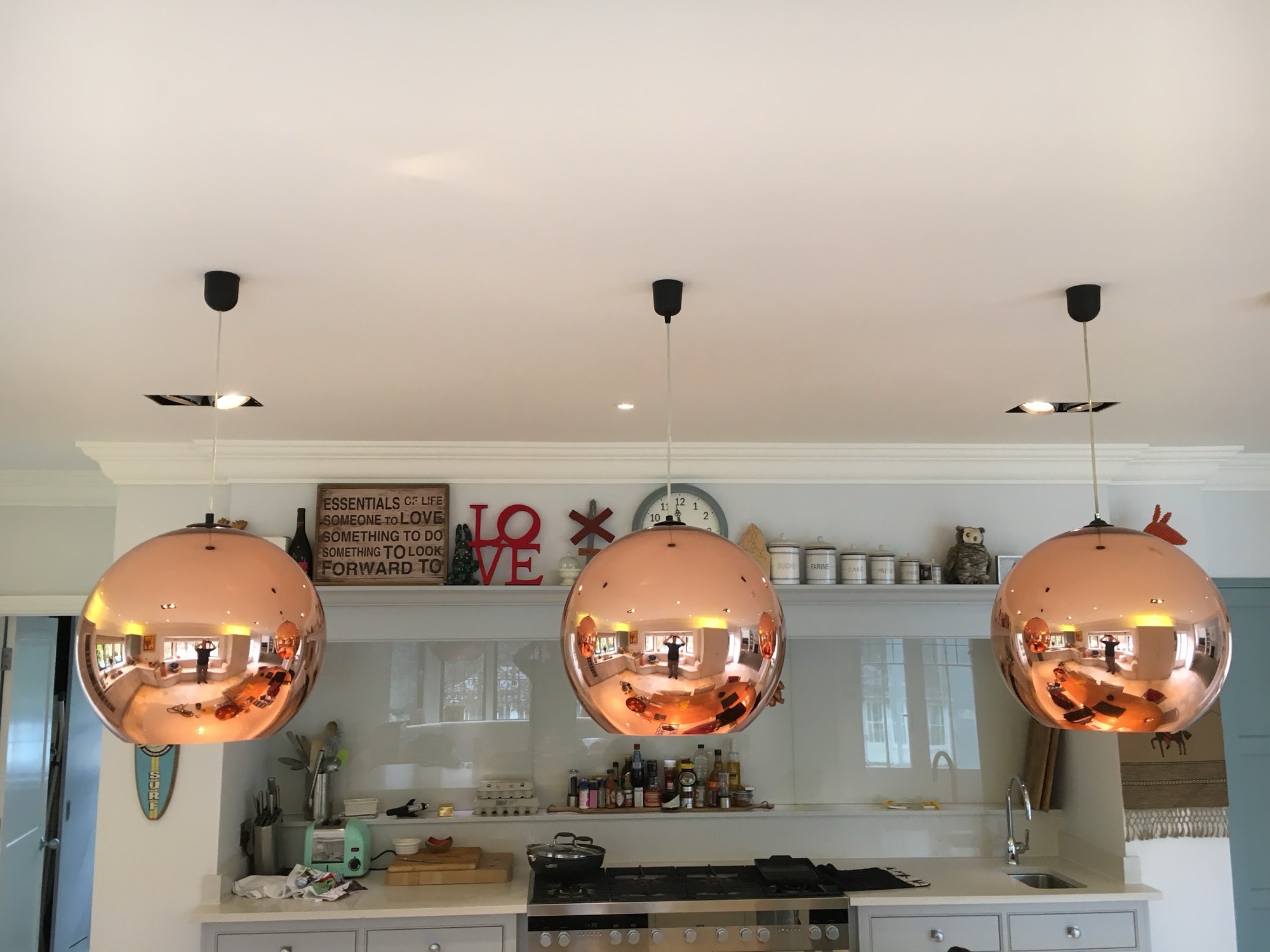 Three copper pendants hung over an island with the drops levelled to the millimetre, and recessed downlights set back so they don't reflect in the shades.
