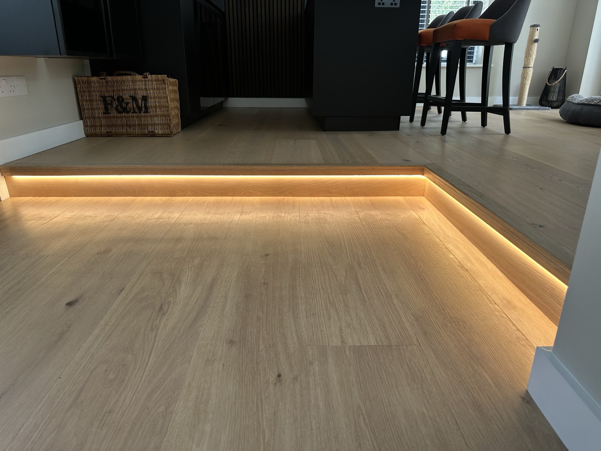 Warm LED strip recessed into the edge of a split-level floor — a lighting detail that has to be cabled at first fix, long before the boards go down.